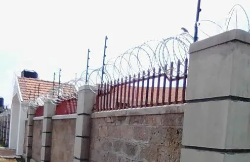 Ornamental iron fencing topped with razor wire on a stone wall